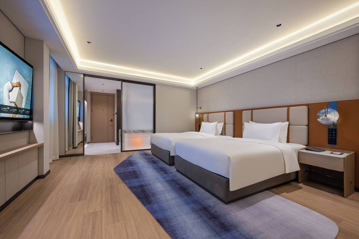 A modern hotel room with a large bed, a TV, and a desk with a lamp.