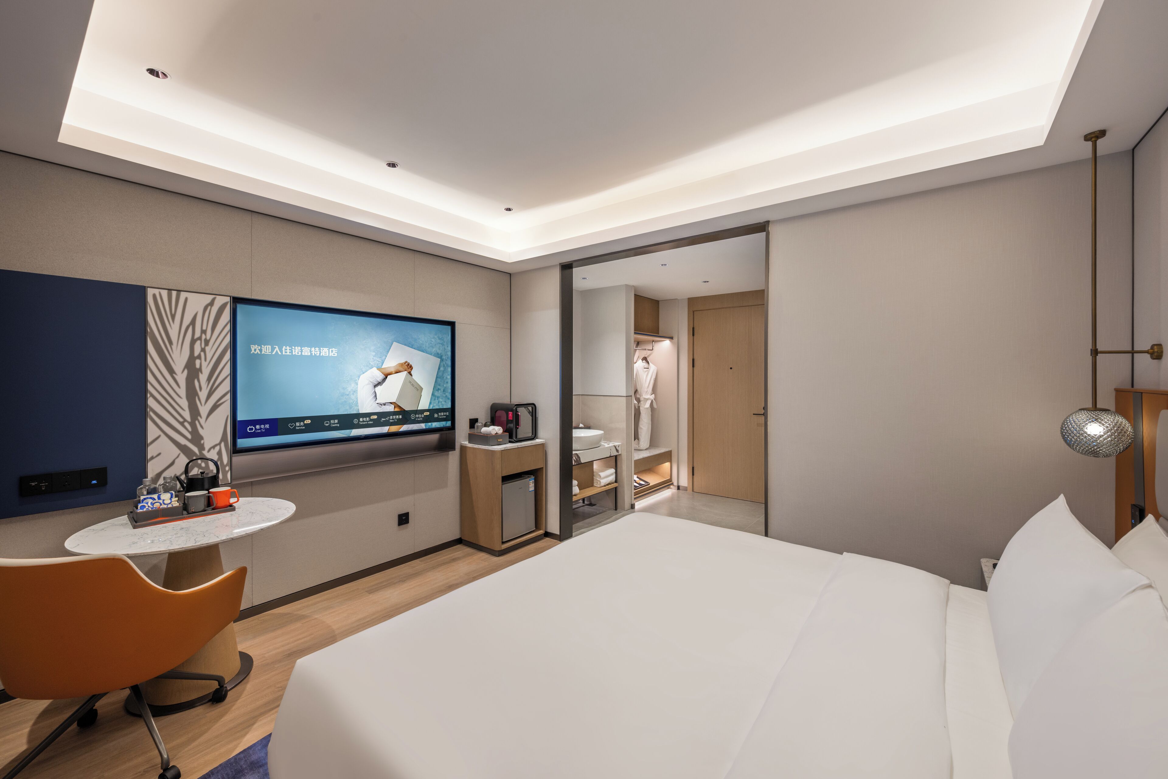 Ein modernes Hotelzimmer mit einem großen Bett, einem an der Wand befestigten Fernseher, einem kleinen Tisch mit Stuhl, einem Schreibtisch und einem Spiegel.