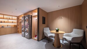 A modern laundry room with built-in washers and dryers, a small table with chairs, and a sign indicating the room's purpose. - Novotel Shanghai Hongqiao International Airport (Shanghai)