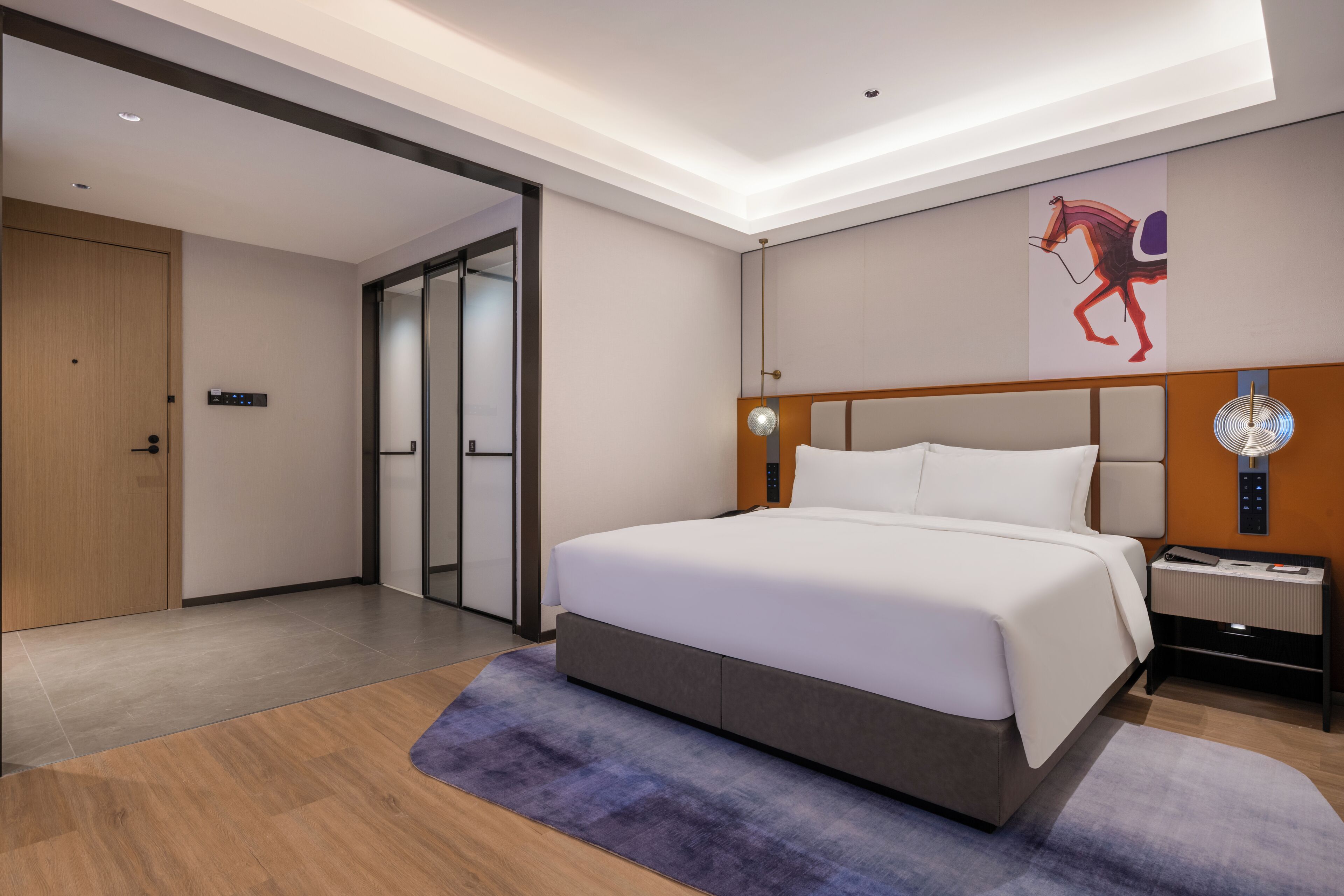 A modern hotel room with a large bed, a nightstand, a wall-mounted clock, and a door leading to another room.