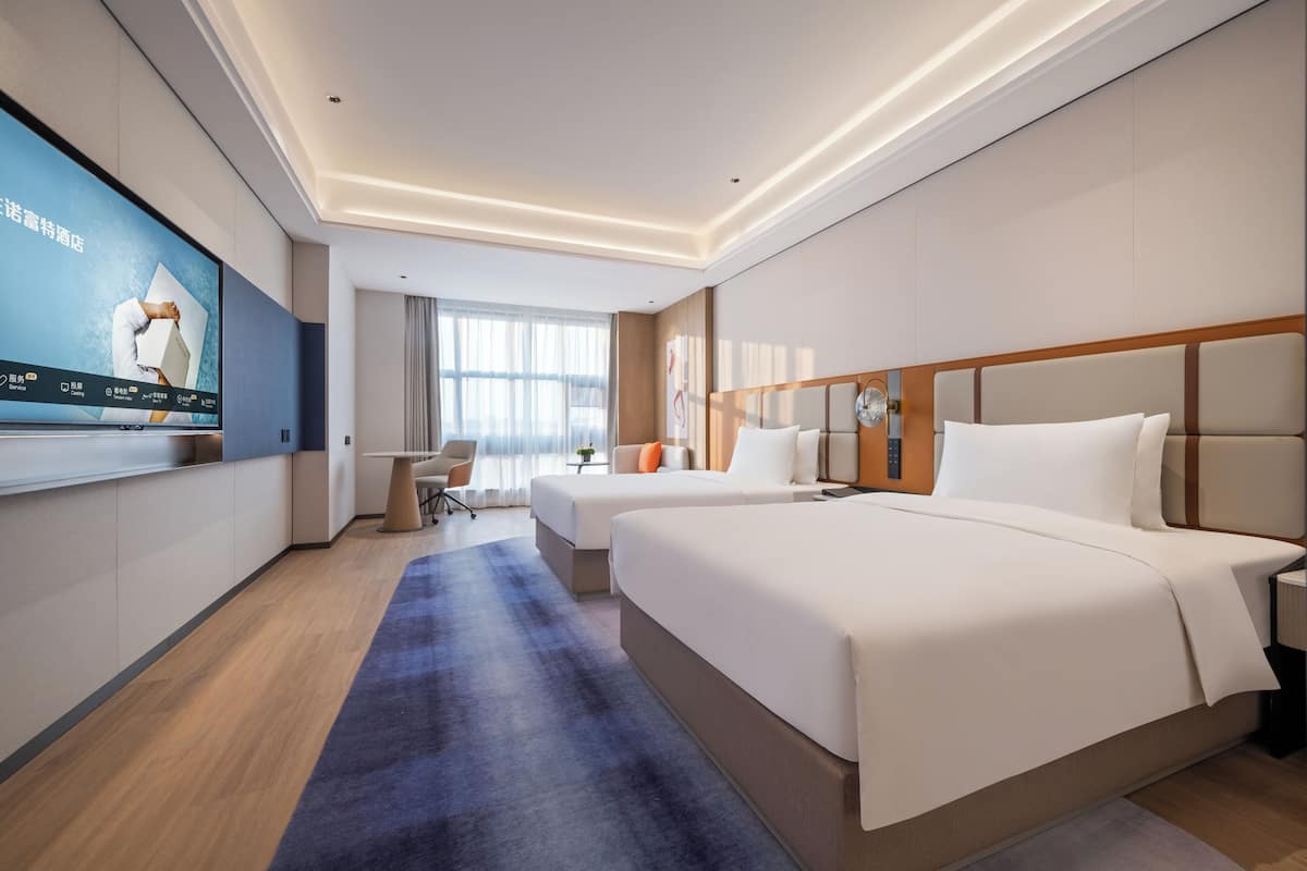 A modern hotel room with two beds, a flat-screen TV, a desk, and a large window.
