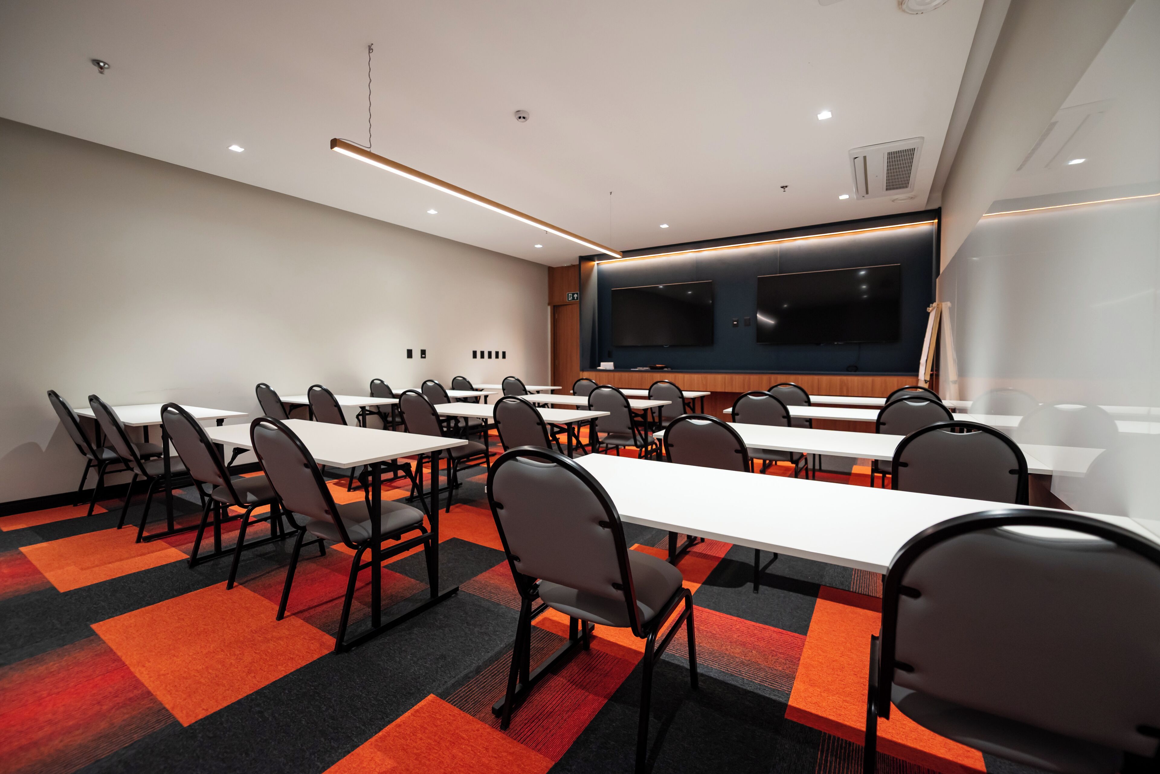 A conference room with multiple tables and chairs, a large screen, and a projector.