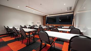 A conference room with multiple tables and chairs, a large screen, and a projector.