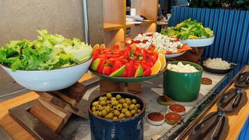 A buffet with various dishes including salads, fruits, and olives.