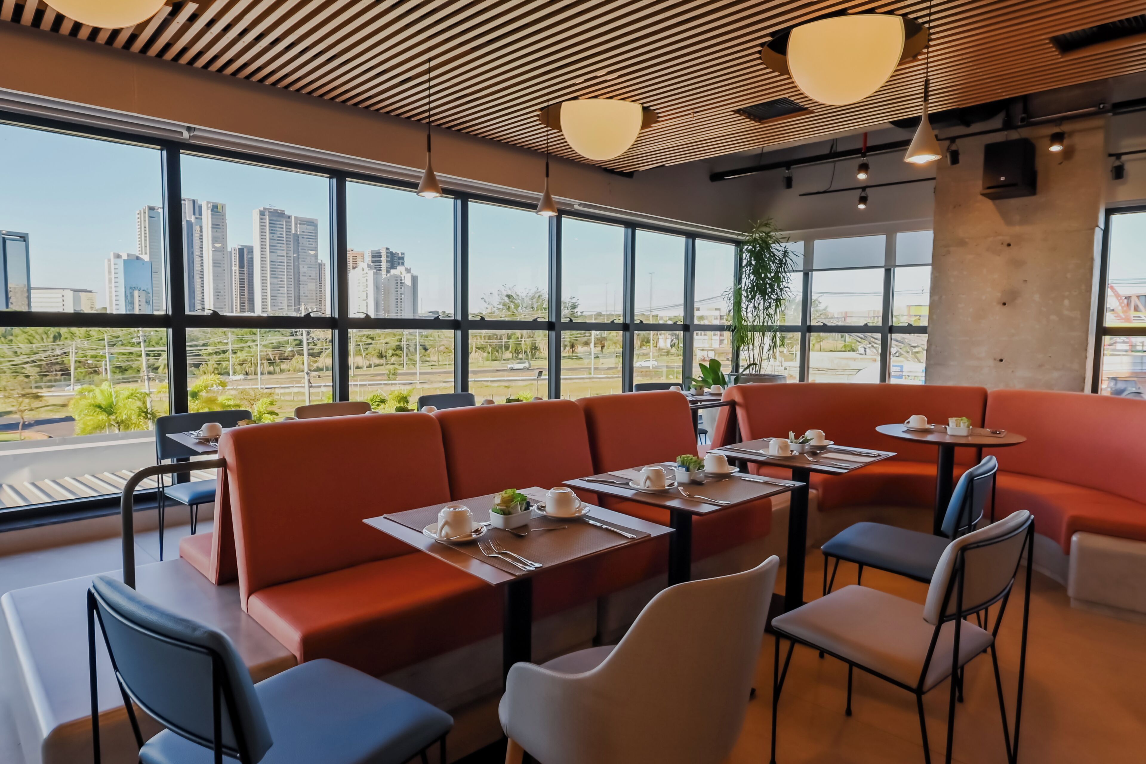 A modern restaurant with high ceilings, large windows, and a view of a cityscape.