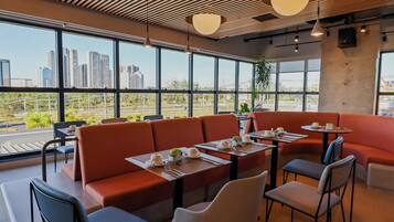 A modern restaurant with high ceilings, large windows, and a view of a cityscape.