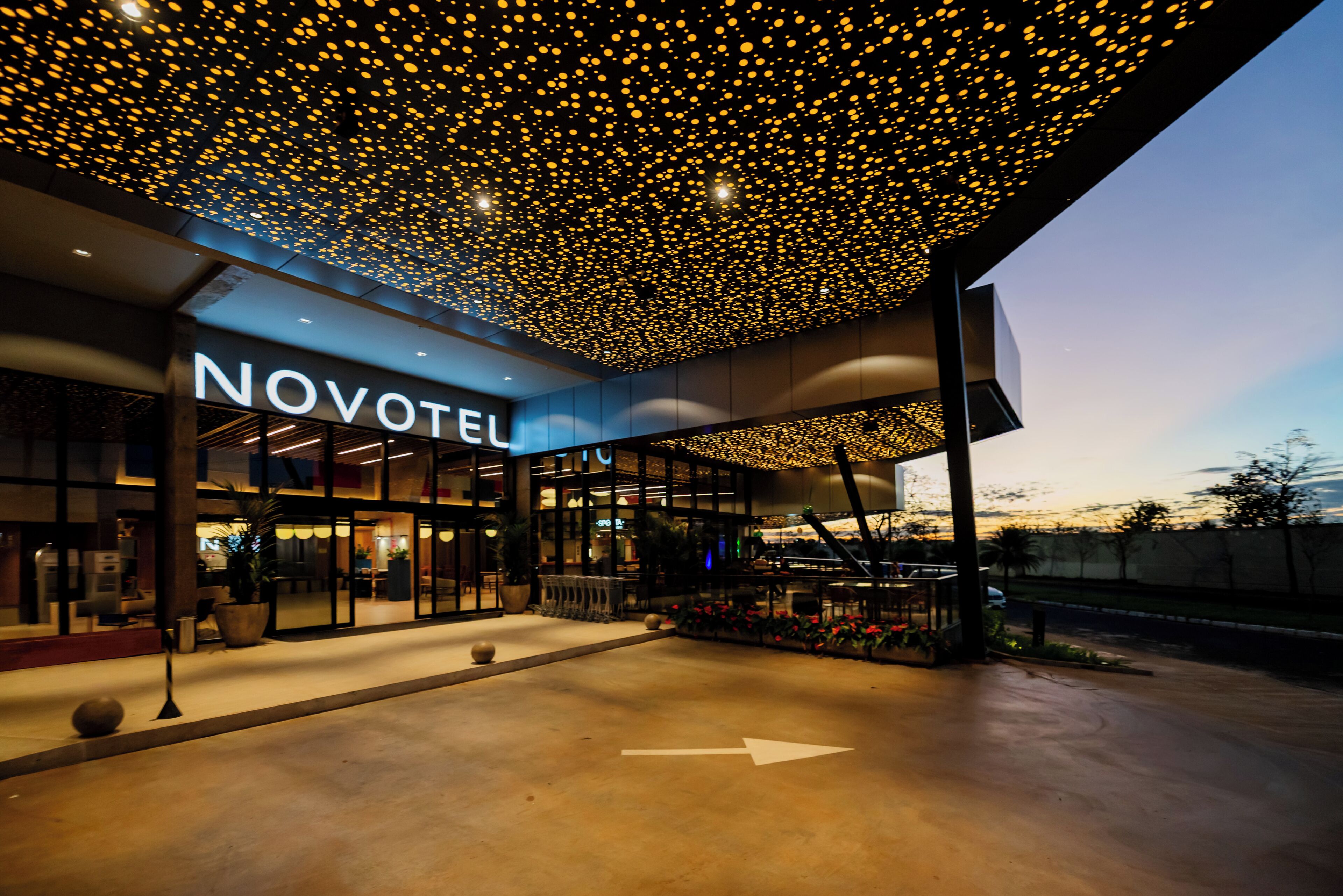 Fachada de hotel con diseño moderno, un letrero que dice 'NOVOTEL' y un techo distintivo con numerosas luces.