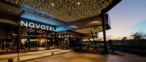 Fachada de hotel con diseño moderno, un letrero que dice 'NOVOTEL' y un techo distintivo con numerosas luces.