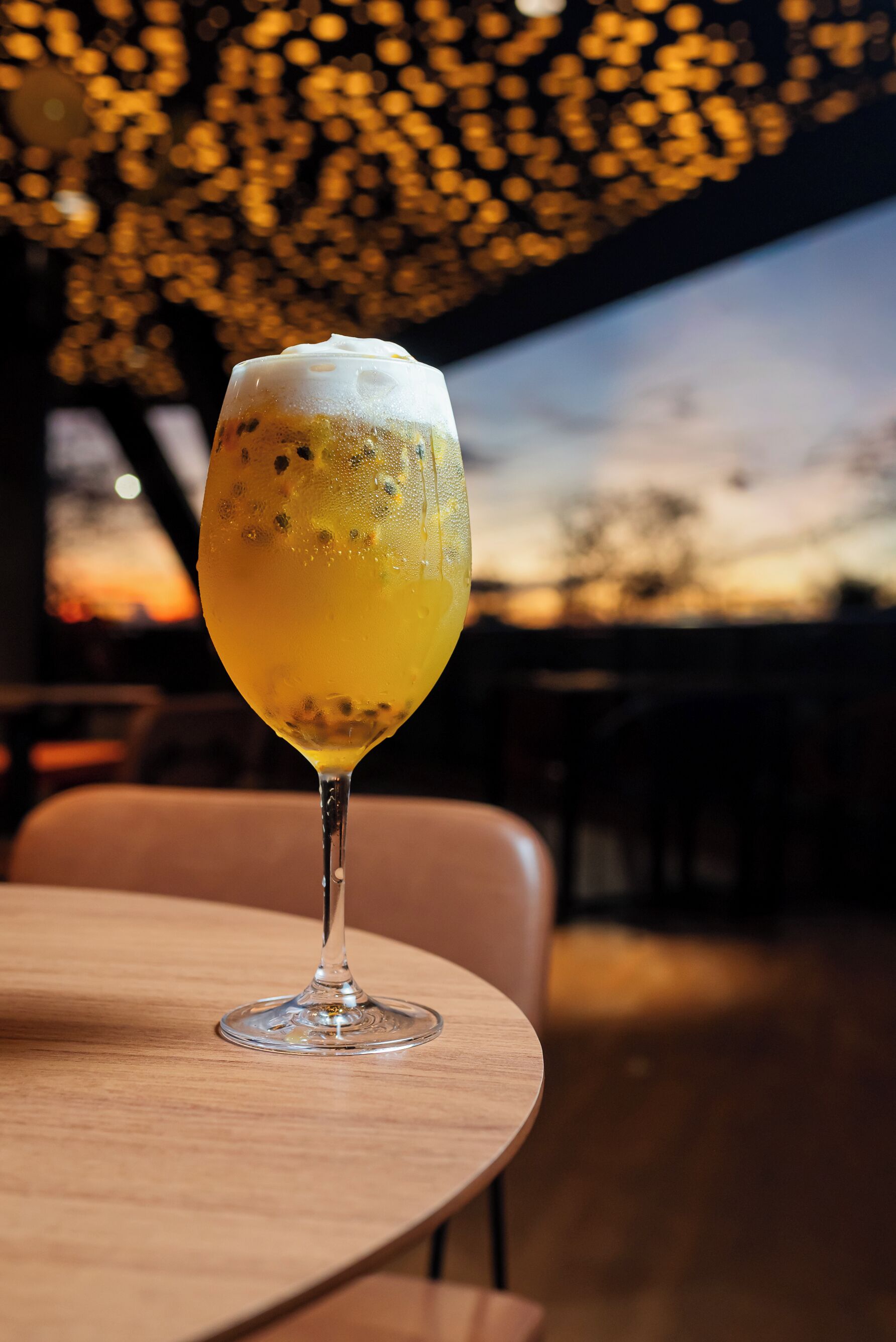 Et glas øl på et træbord med solnedgang i baggrunden.