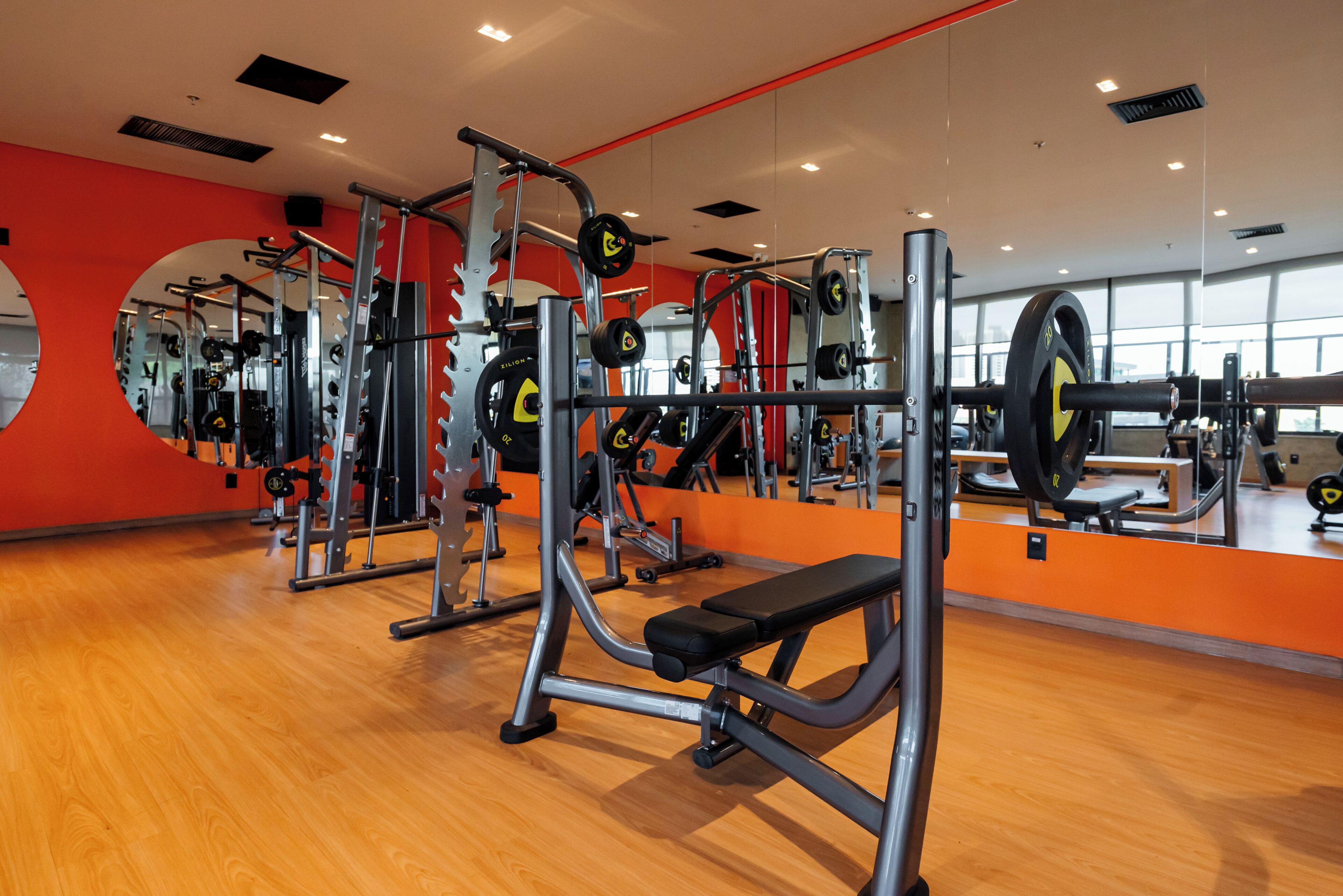 A gym with various exercise equipment, wooden flooring, and mirrors on the walls.