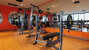 A gym with various exercise equipment, wooden flooring, and mirrors on the walls.