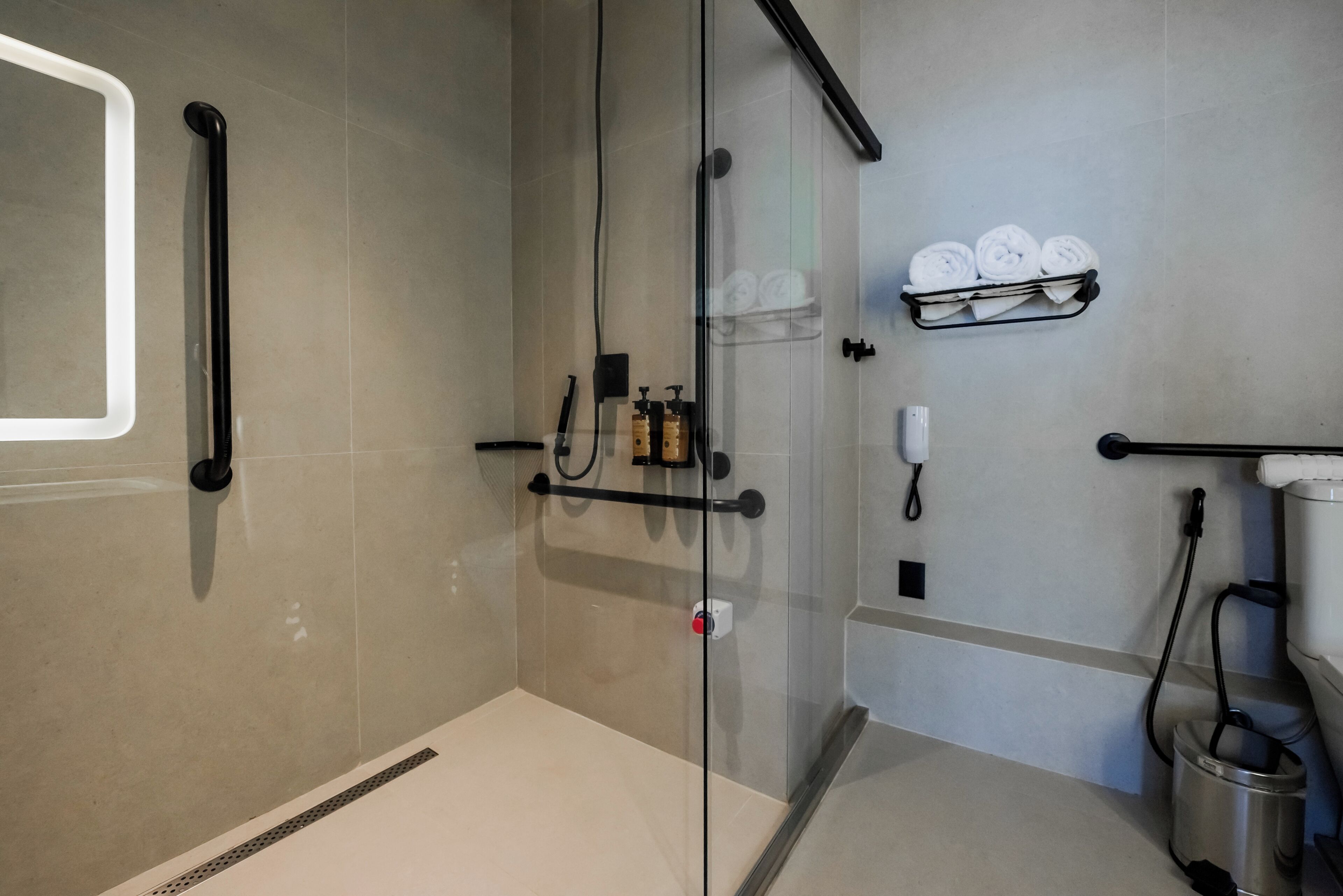 Une salle de bain moderne avec une douche à parois de verre, un porte-serviettes avec des serviettes pliées, un distributeur de savon et une douchette à main.