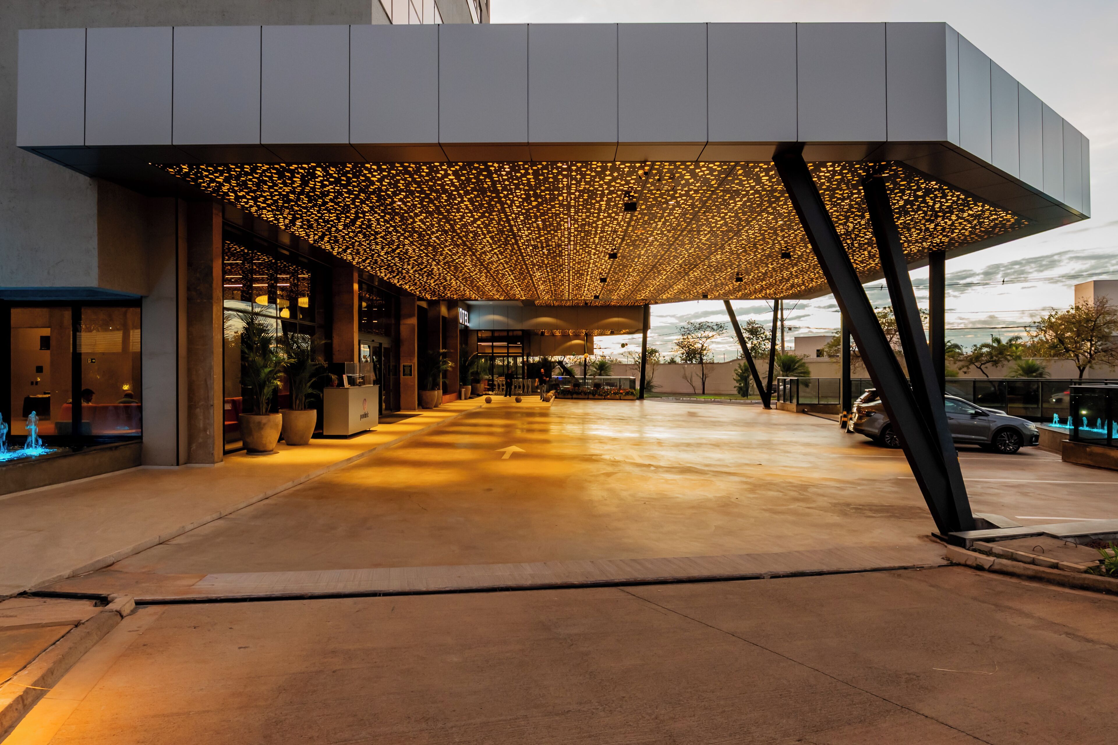 Entrada de hotel com galeria coberta, vasos de plantas e céu claro.