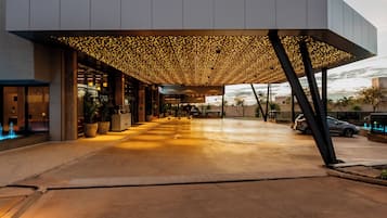 Entrada de hotel com galeria coberta, vasos de plantas e céu claro.