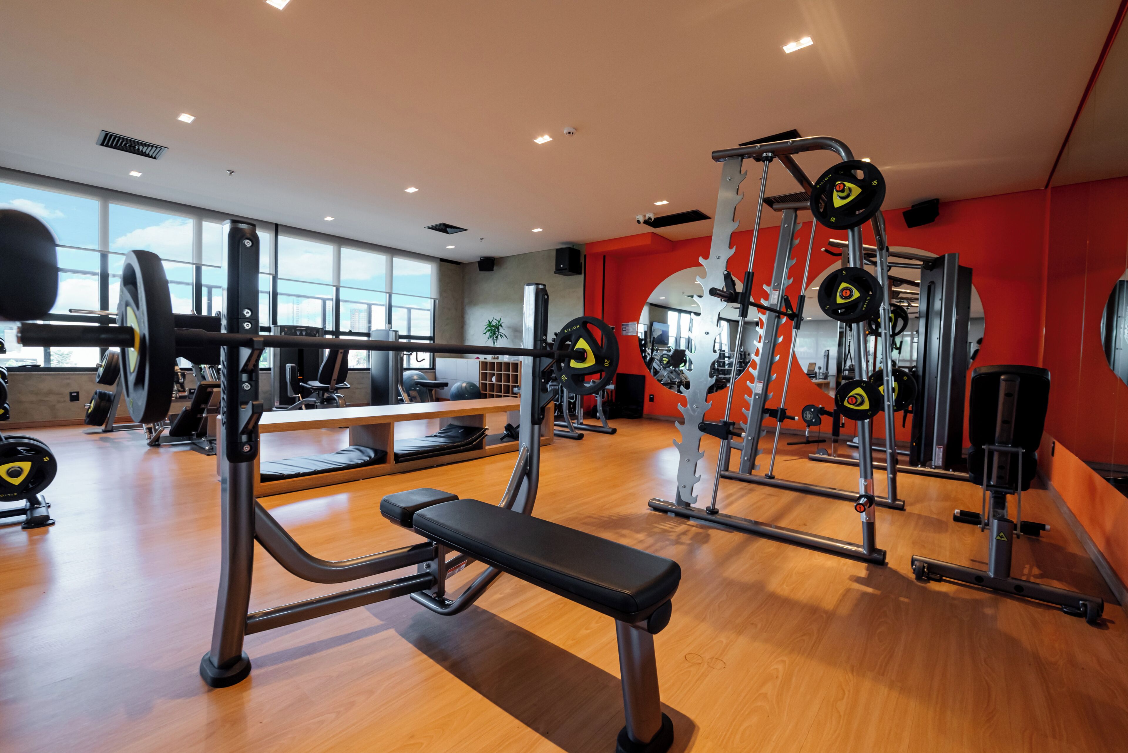 A gym with various exercise equipment, a bench, and a mirror.