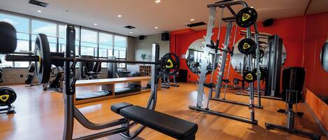 A gym with various exercise equipment, a bench, and a mirror.