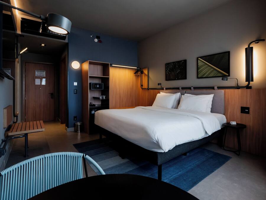 Una habitación de hotel moderna con una cama grande, un escritorio, una silla y una mesita.