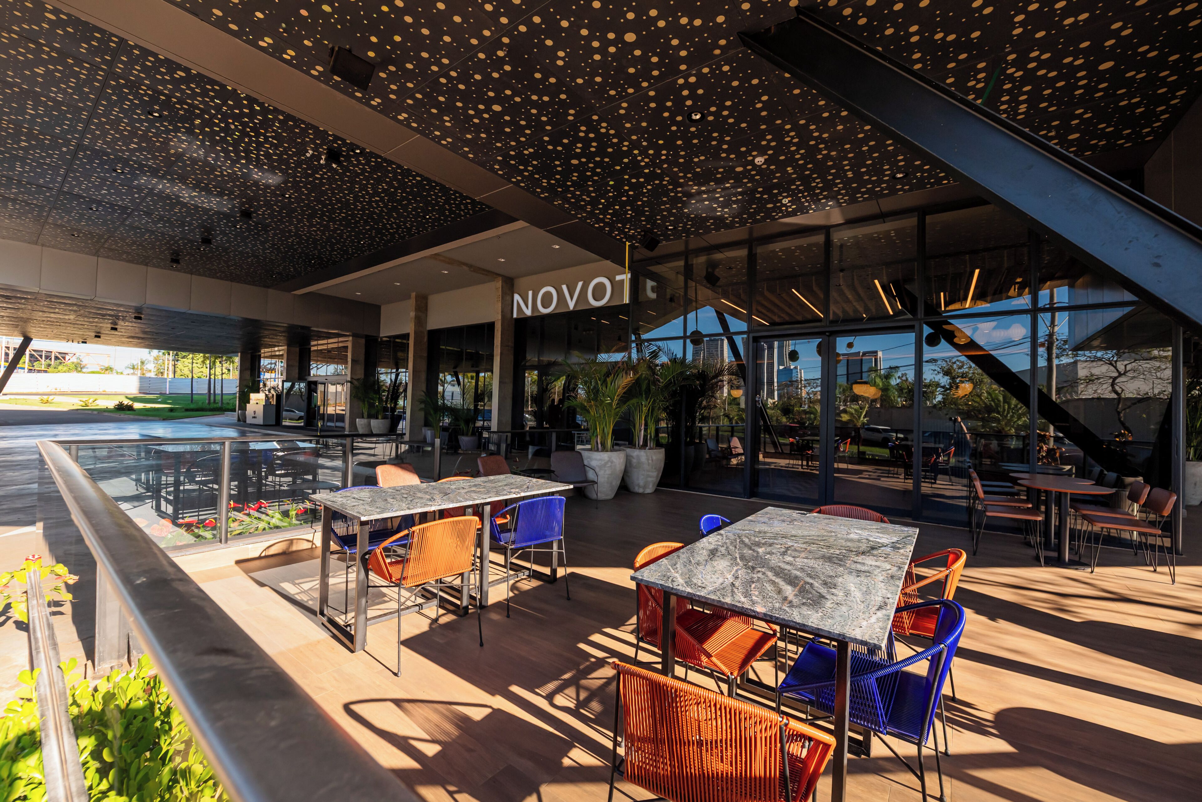 Área externa com mesas e cadeiras, design de teto moderno e fachada visível com a inscrição 'NOVOT'.