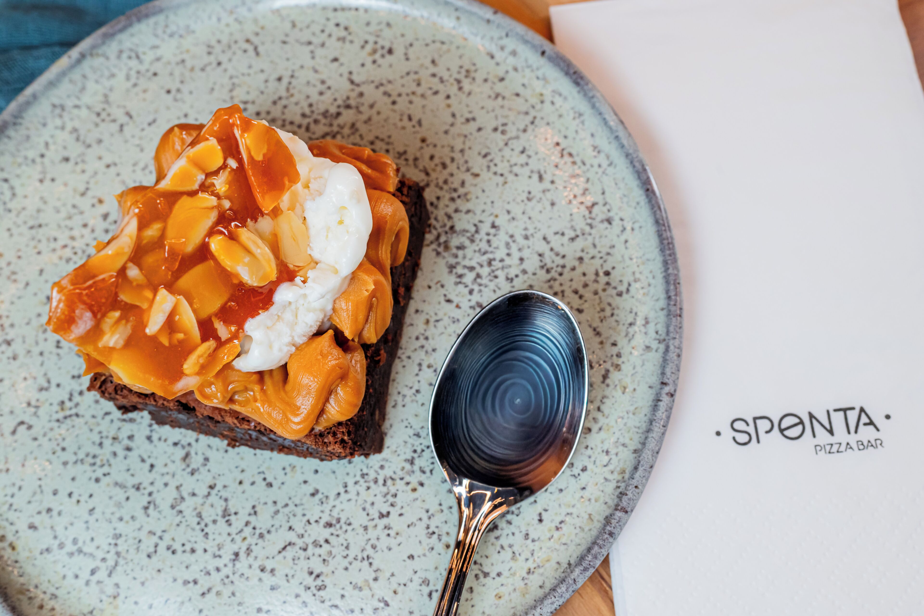 A slice of pie with caramel and whipped cream on a plate, accompanied by a spoon.