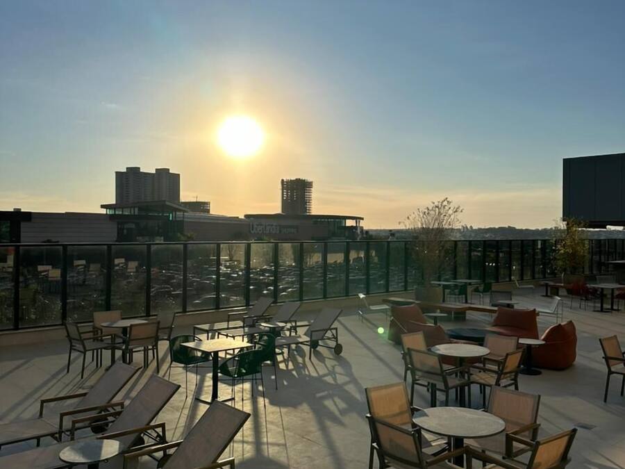 Een dakterras met buitenmeubilair, een helder uitzicht op de skyline van de stad, en een ondergaande zon op de achtergrond.