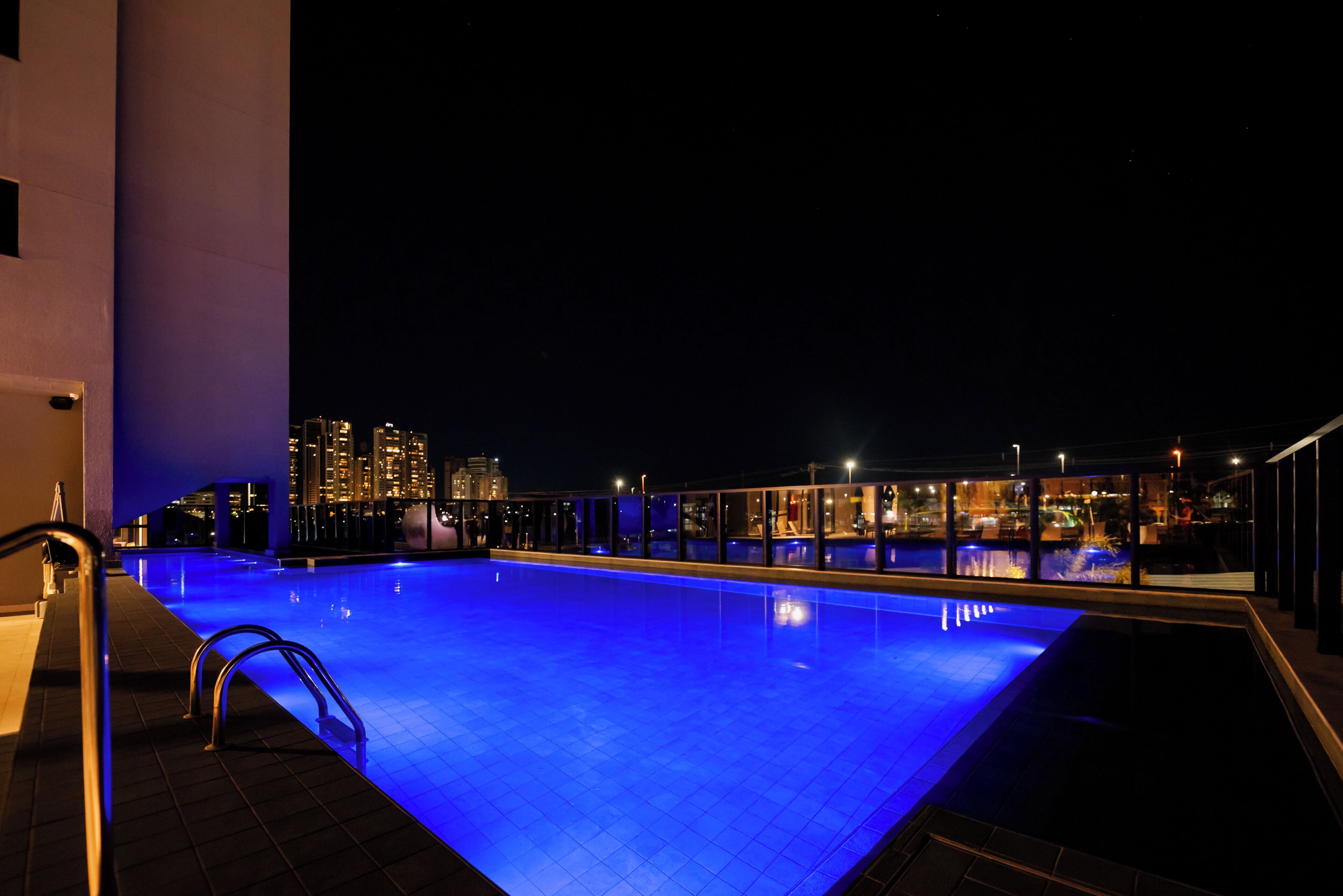 A nighttime view of a rooftop swimming pool with city lights in the background.