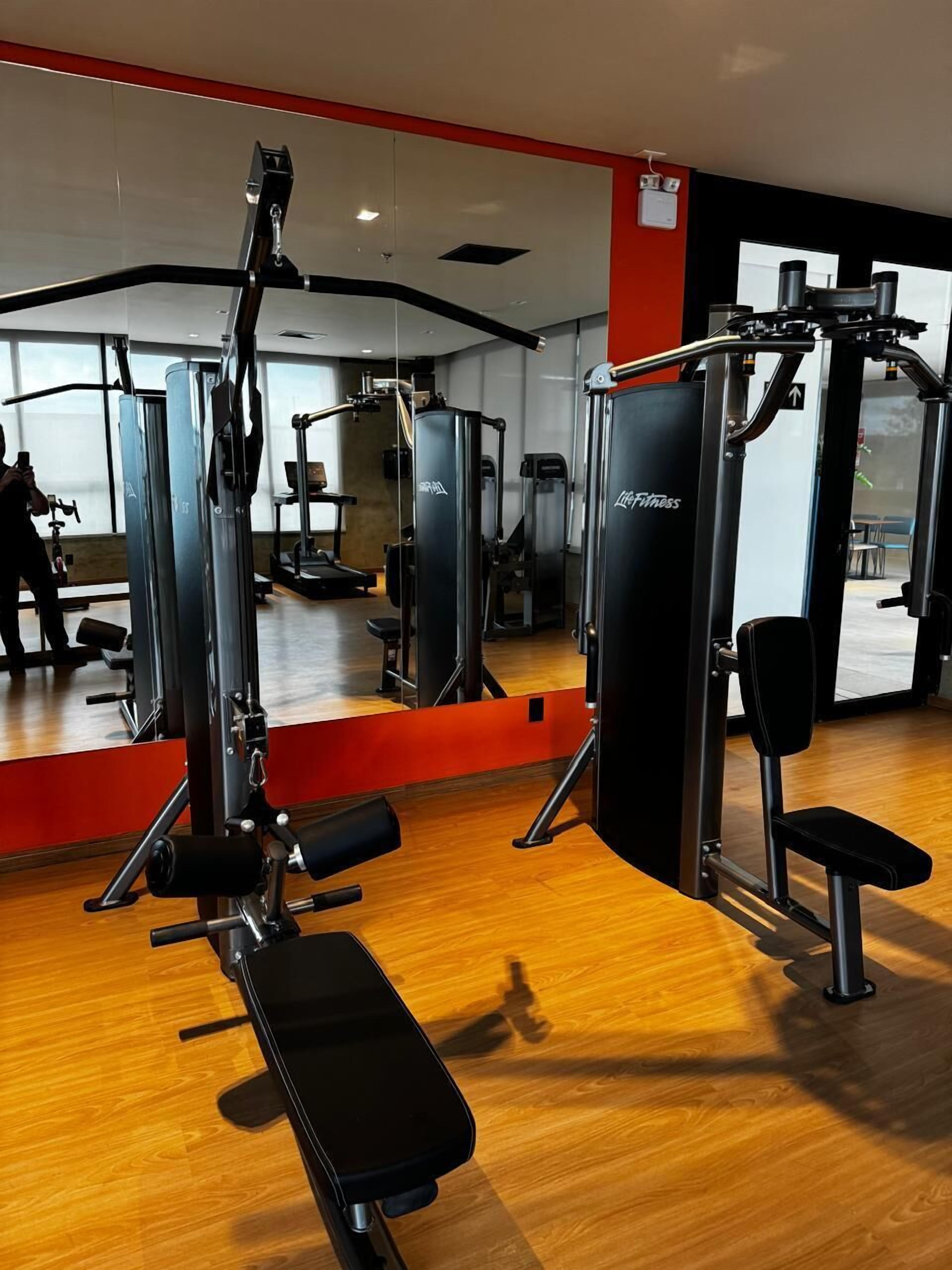 Ett gym med olika träningsmaskiner, en bänk och en spegel.
