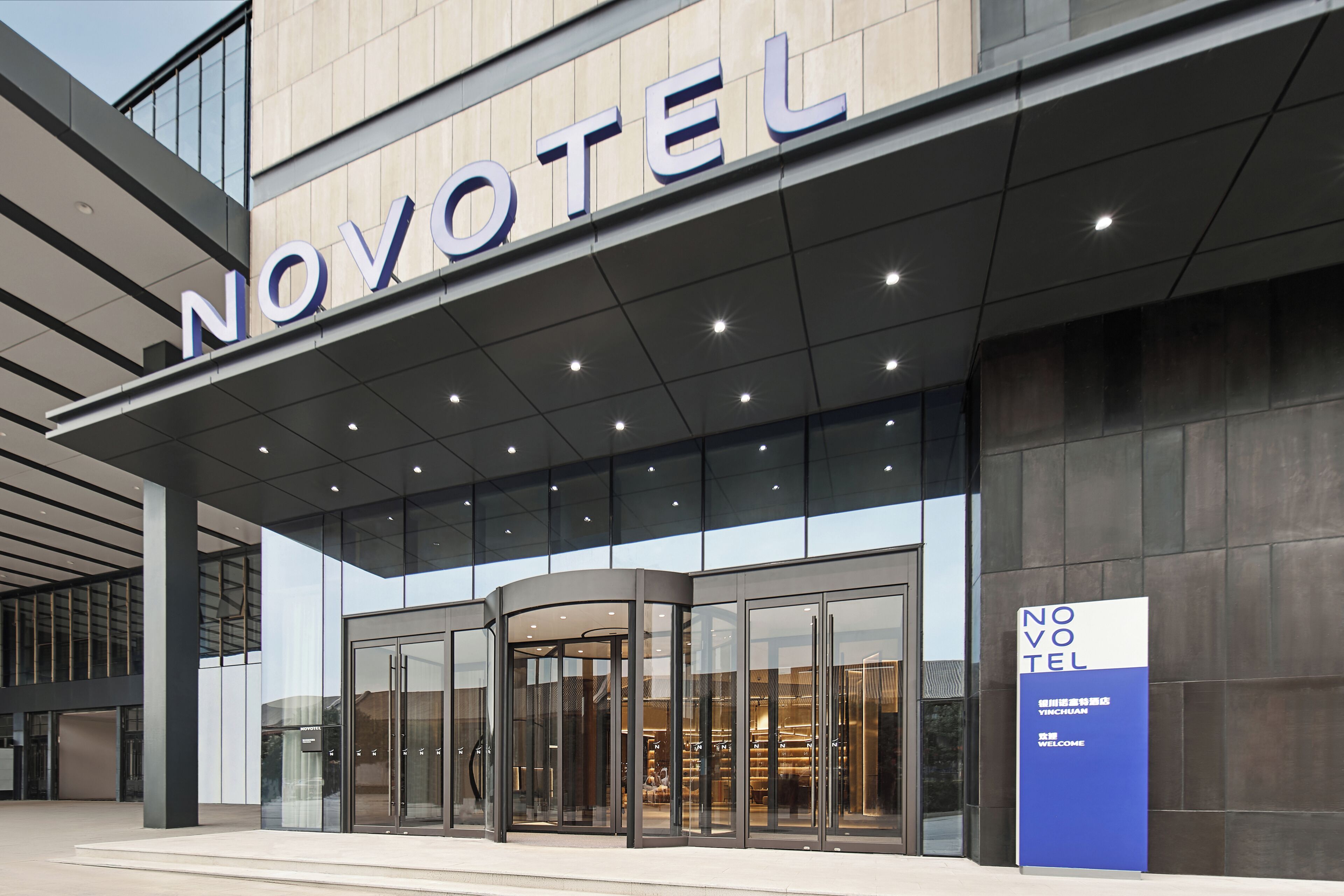 A hotel entrance with a revolving door, large glass windows, and a signboard.