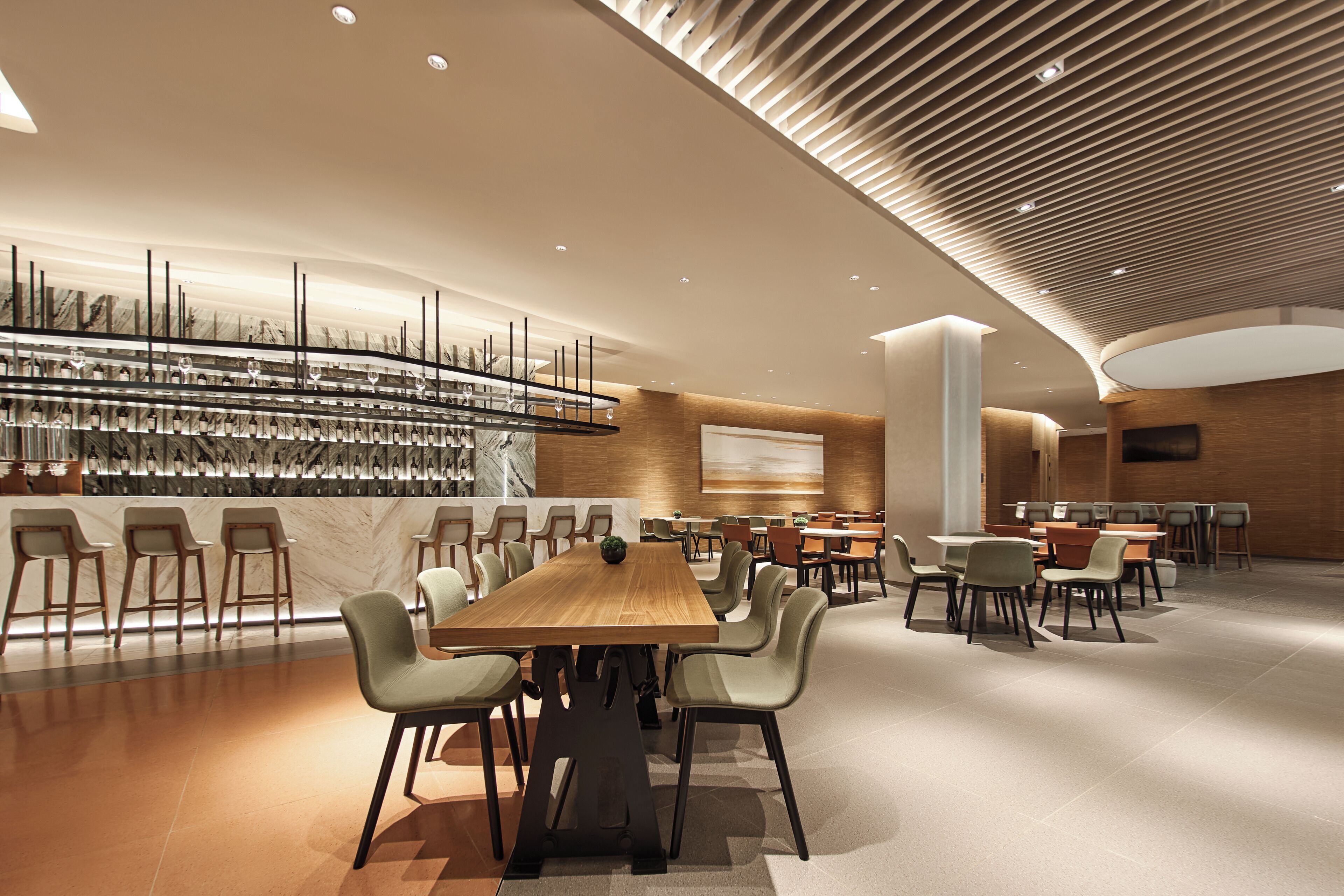 A modern dining area with a long wooden table surrounded by chairs, a wall-mounted wine rack, and a curved ceiling design.