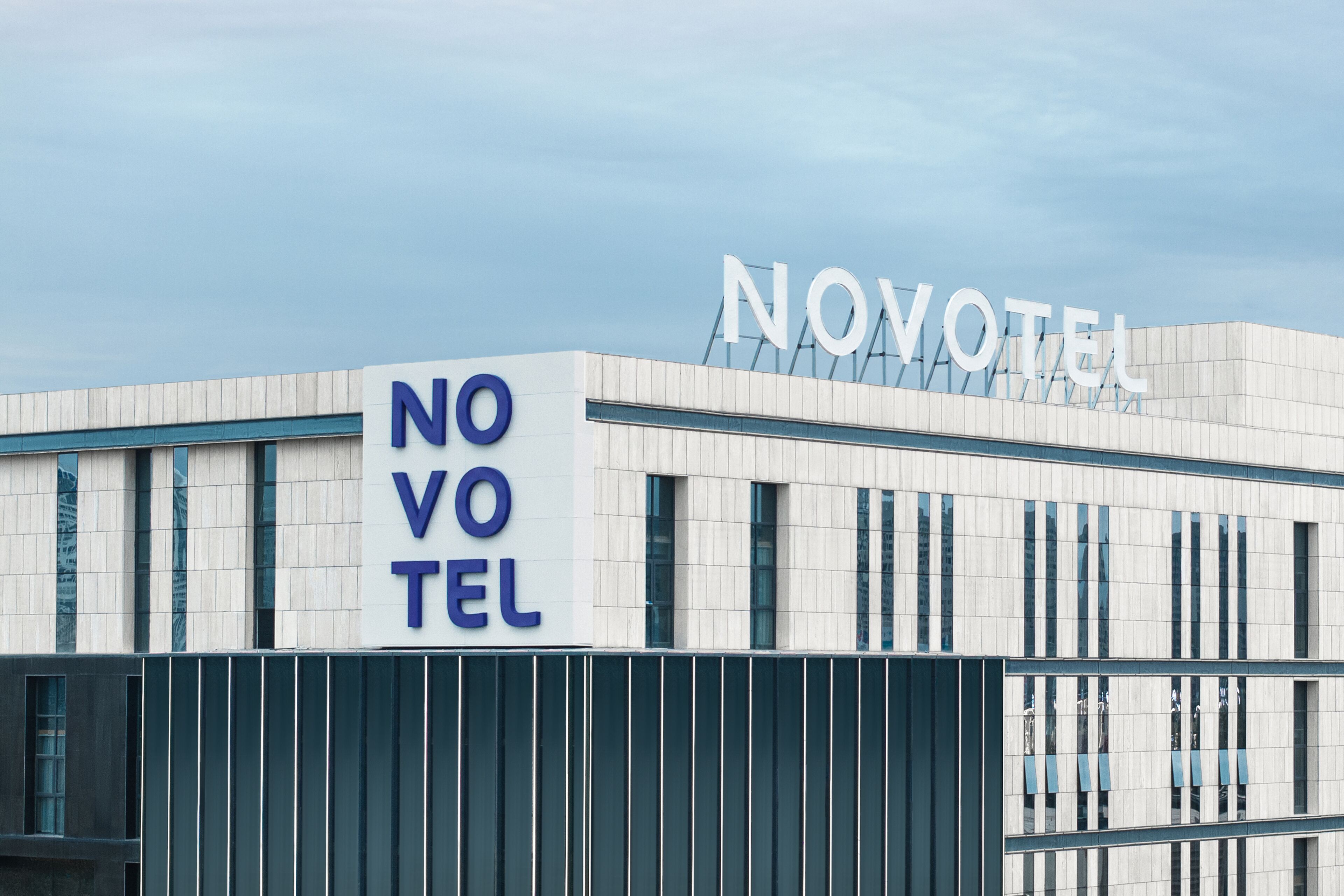 A modern hotel with a prominent 'NOVOTEL' sign, large windows, and a clean, contemporary design.