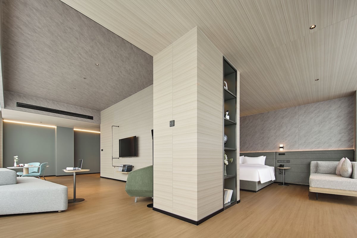 Une chambre d’hôtel moderne équipée d’un canapé, d’un lit, d’un bureau, d’une télévision et d’une étagère fixée au mur.