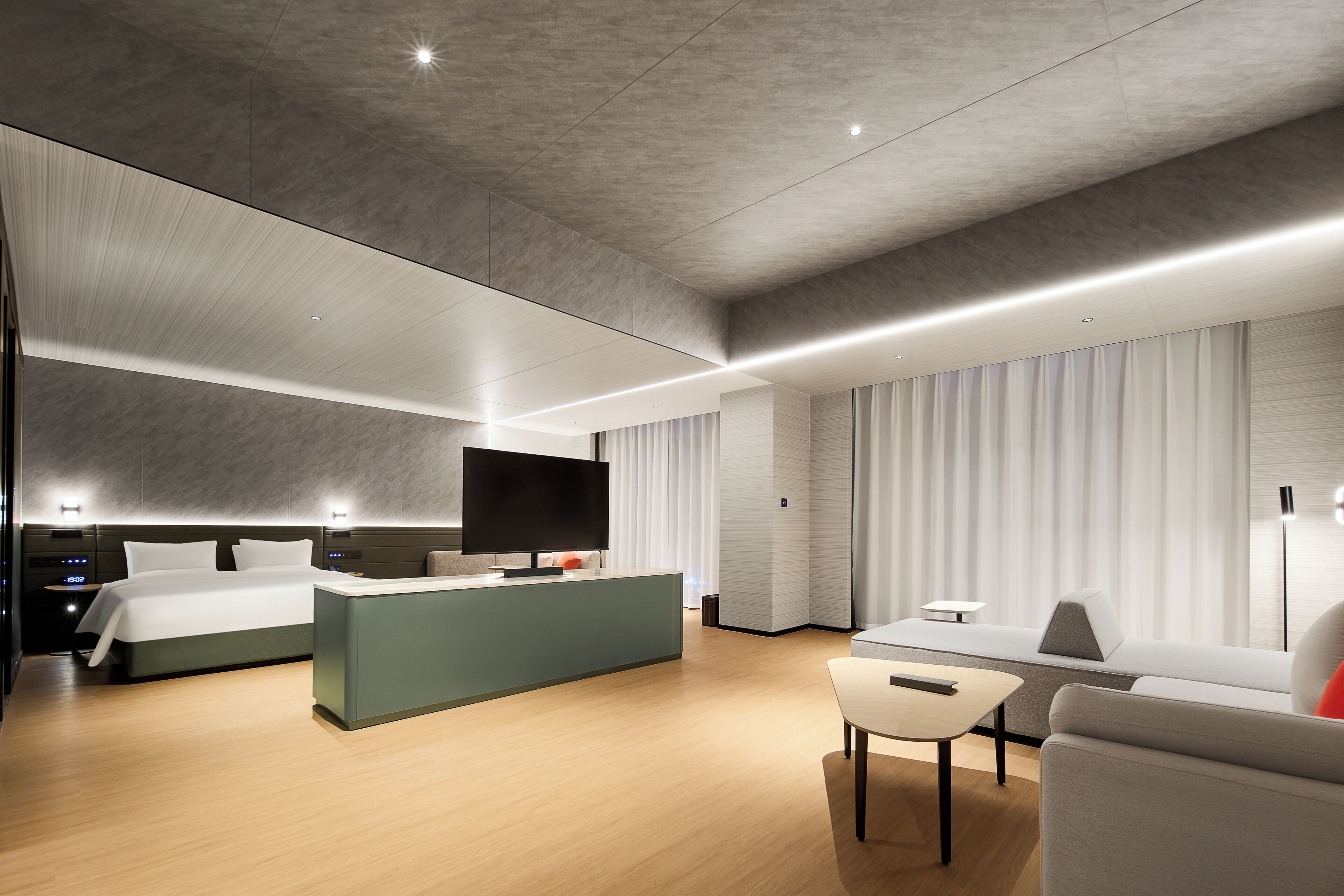 A modern hotel room with a bed, a desk, a sofa, and a TV.