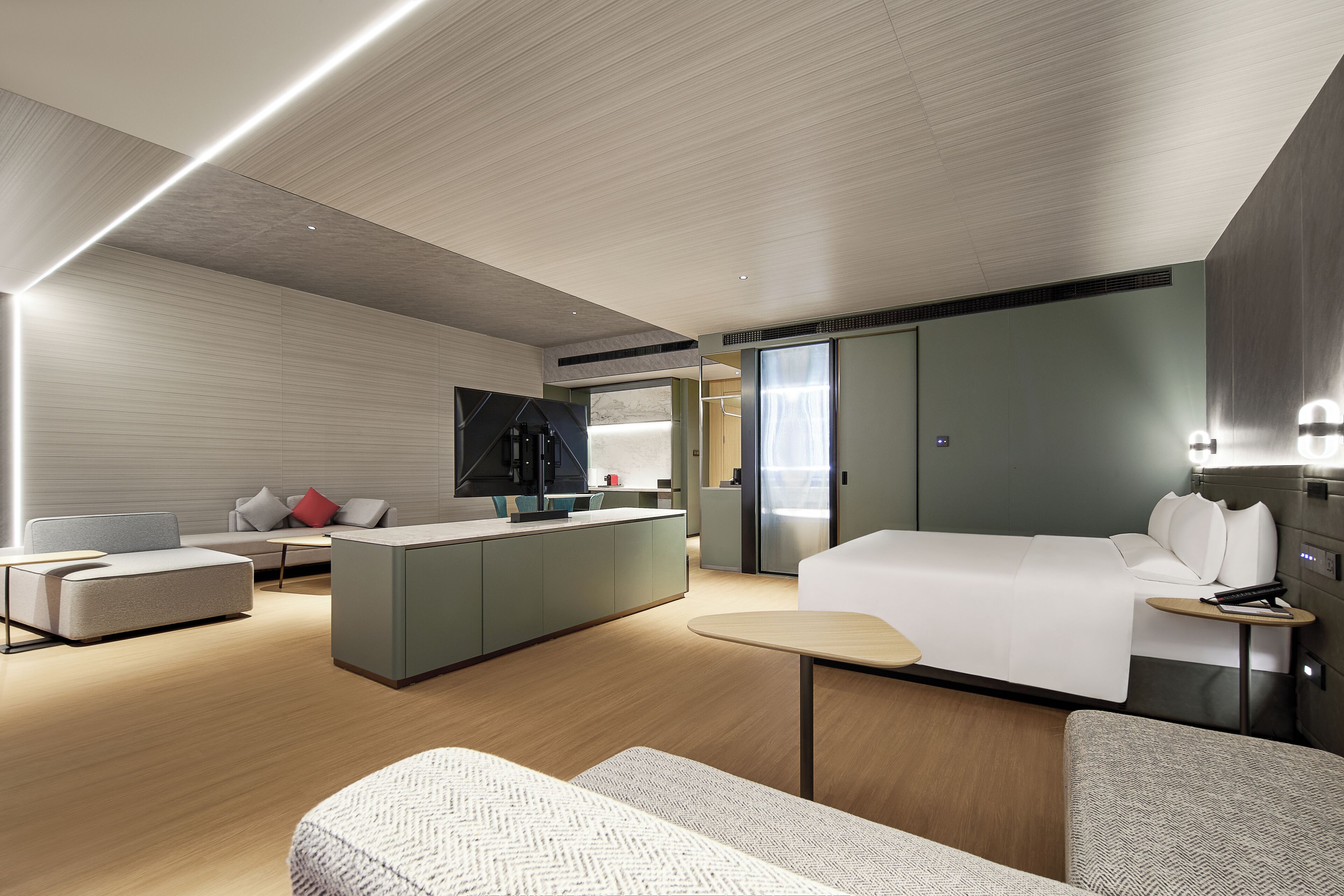 A modern hotel room with a central island, a bed, a sofa, and a small table.
