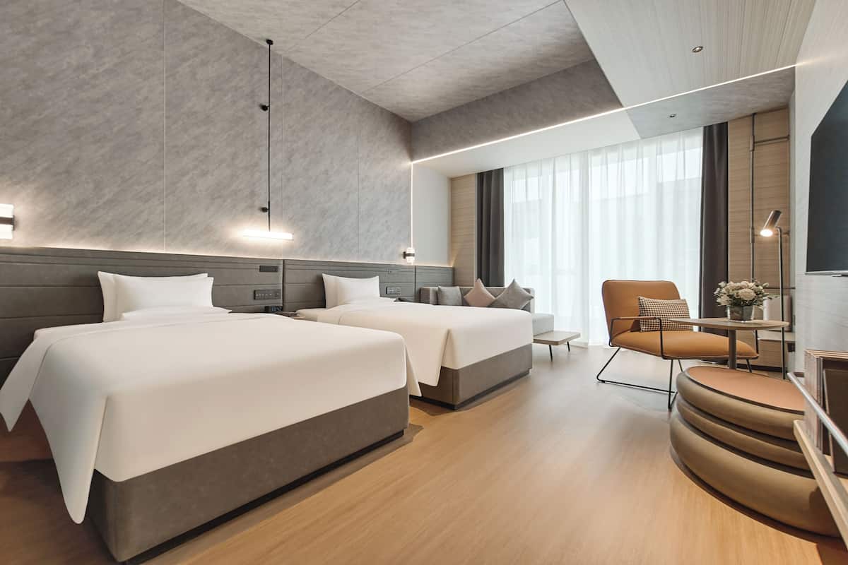 Une chambre d’hôtel moderne avec deux lits, un canapé, un fauteuil et une petite table.