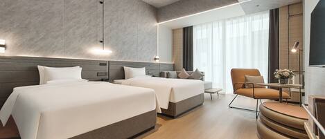 A modern hotel room with two beds, a sofa, a chair, and a small table.