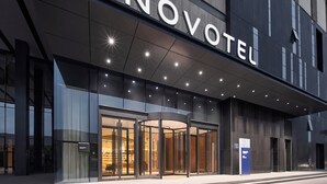 Ein moderner Hotelzugang mit einer Drehtür, Glasfassade und beleuchteter Beschilderung.