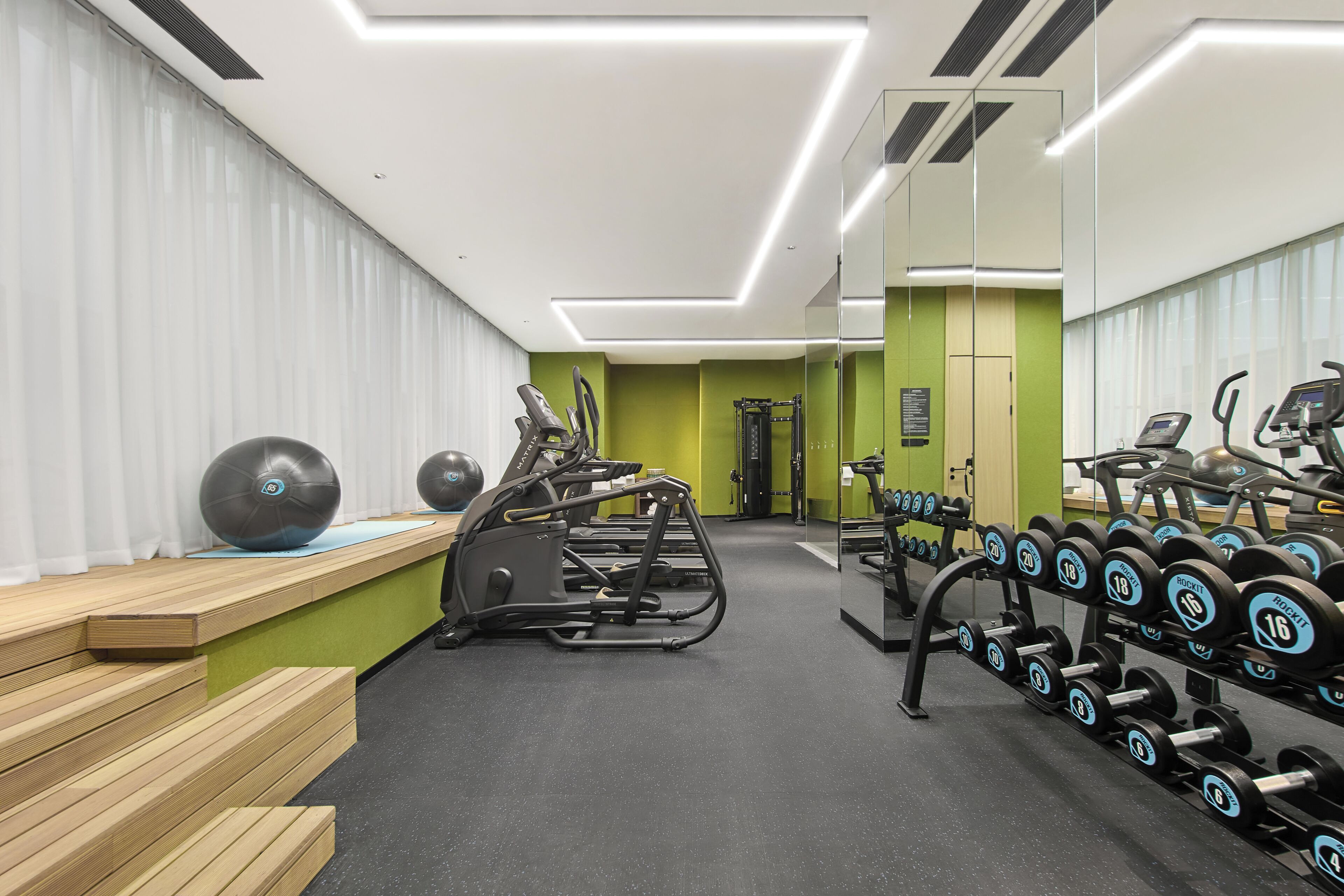 Una palestra con attrezzature per esercizi, panche e uno specchio lungo la parete.