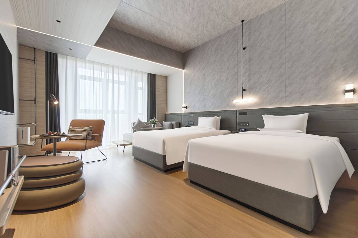 Une chambre d’hôtel moderne avec deux lits, un coin salon et une grande fenêtre.