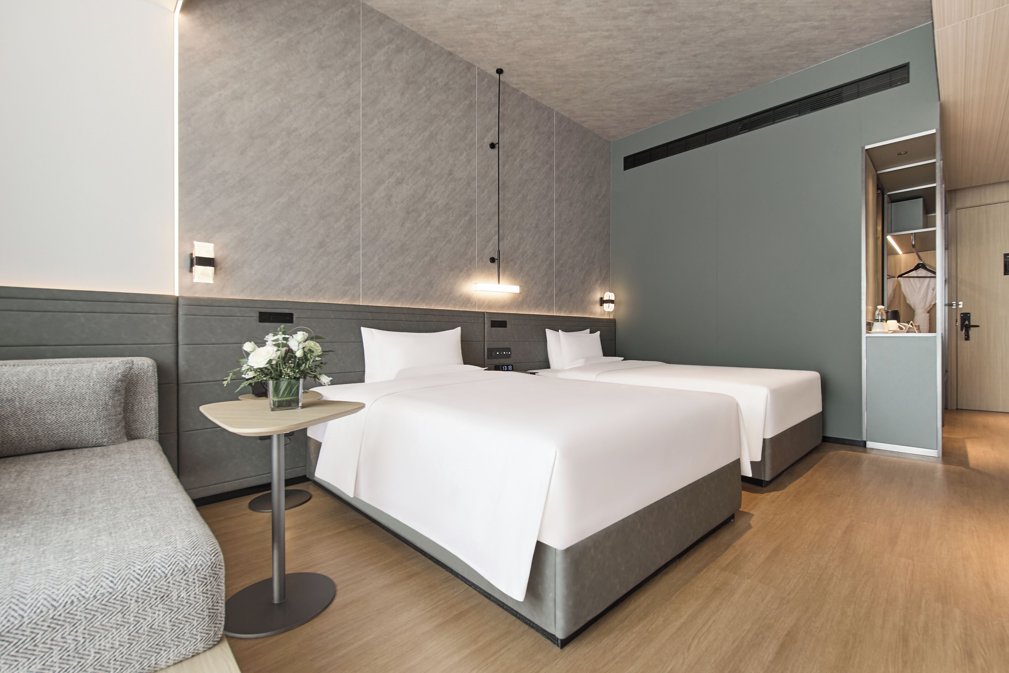 A modern hotel room with a large bed, bedside tables, a small table with flowers, and a wardrobe.
