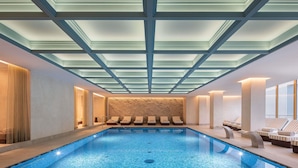 A modern indoor swimming pool with a glass ceiling, lounge chairs, and a stone wall. - Swissôtel Marianske Lazne - Opened in December 2025 (Marianske Lazne)