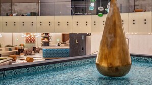 A modern indoor pool with a unique conical water feature, a bar area, and a seating lounge. - Swissôtel Marianske Lazne - Opened in December 2025 (Marianske Lazne)
