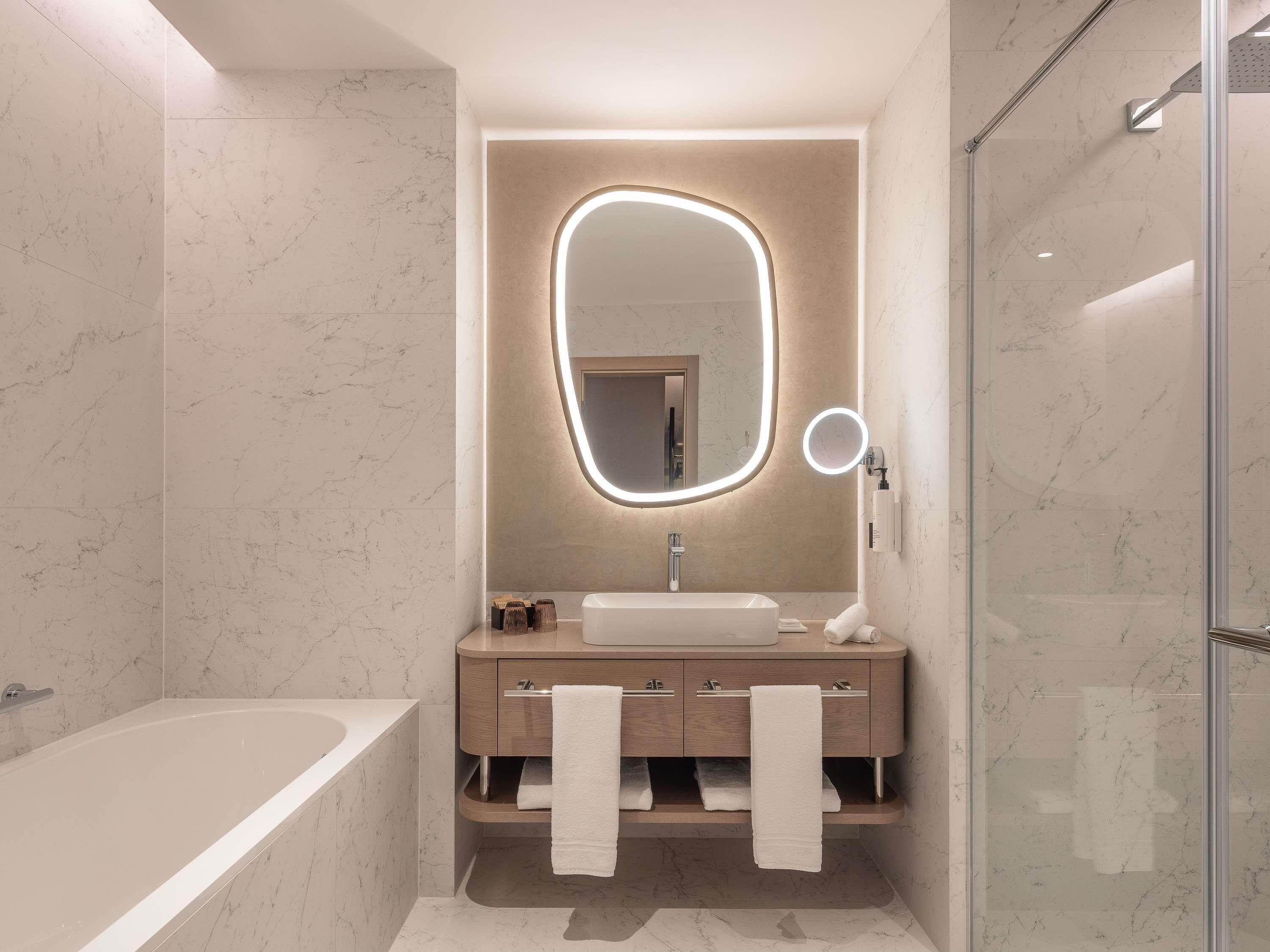 A modern bathroom with a marble floor, a freestanding bathtub, a vanity with a mirror, and a glass shower enclosure.