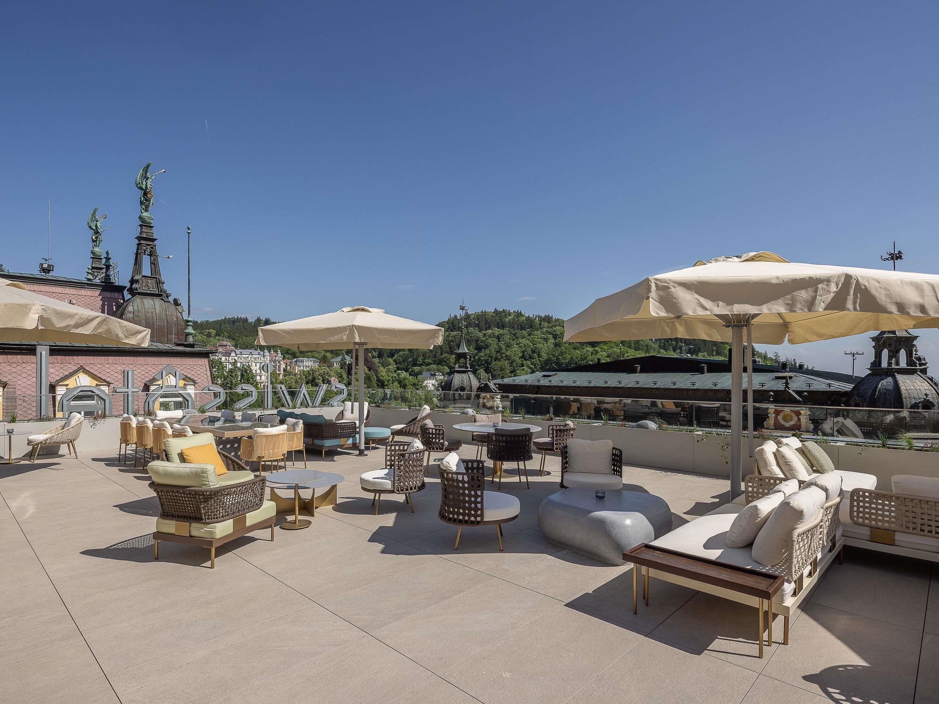 An outdoor seating area with various chairs and tables, umbrellas, and a view of a historic building with spires.