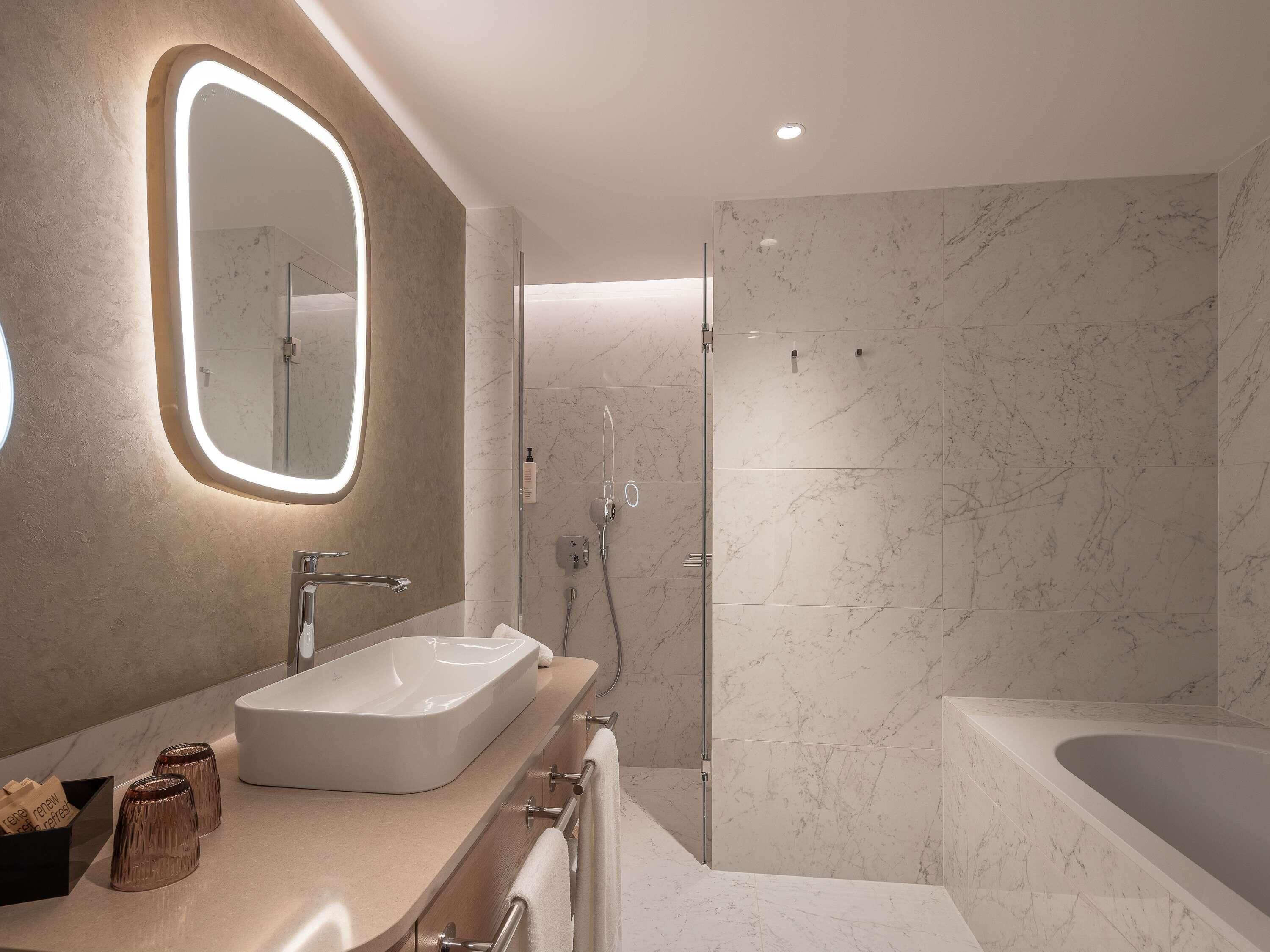 A modern bathroom with a large mirror, a sink, a shower, and a bathtub.
