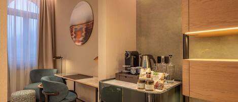 Quarto de hotel moderno com escrivaninha de vidro, sofá, poltrona, tapete estampado e um espelho grande.