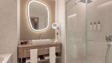 A modern bathroom with a large oval mirror, a glass-enclosed shower, and a vanity with a sink and towel rack.