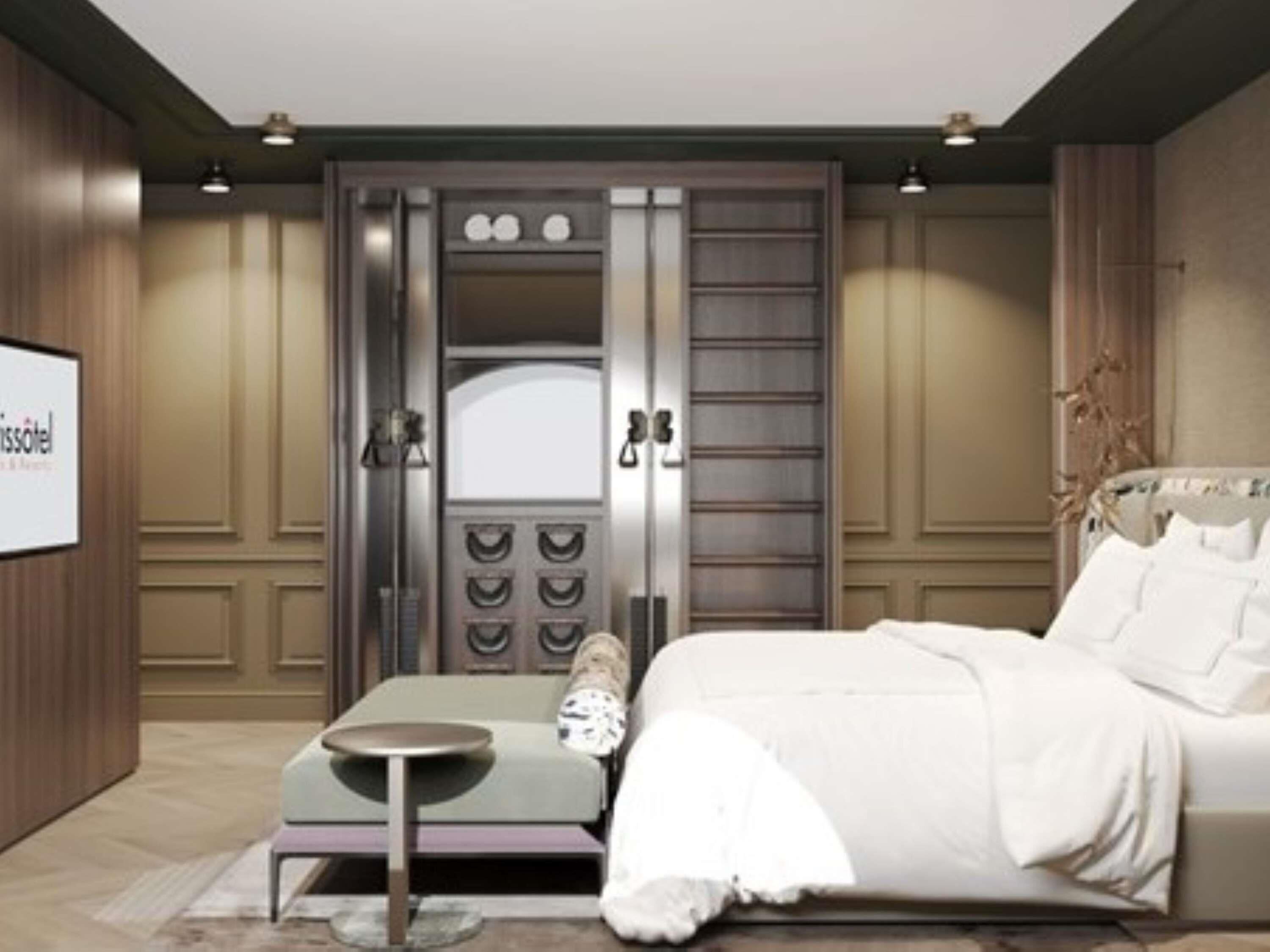 A hotel room with a bed, a small round table, a bench, and a wardrobe with multiple doors.