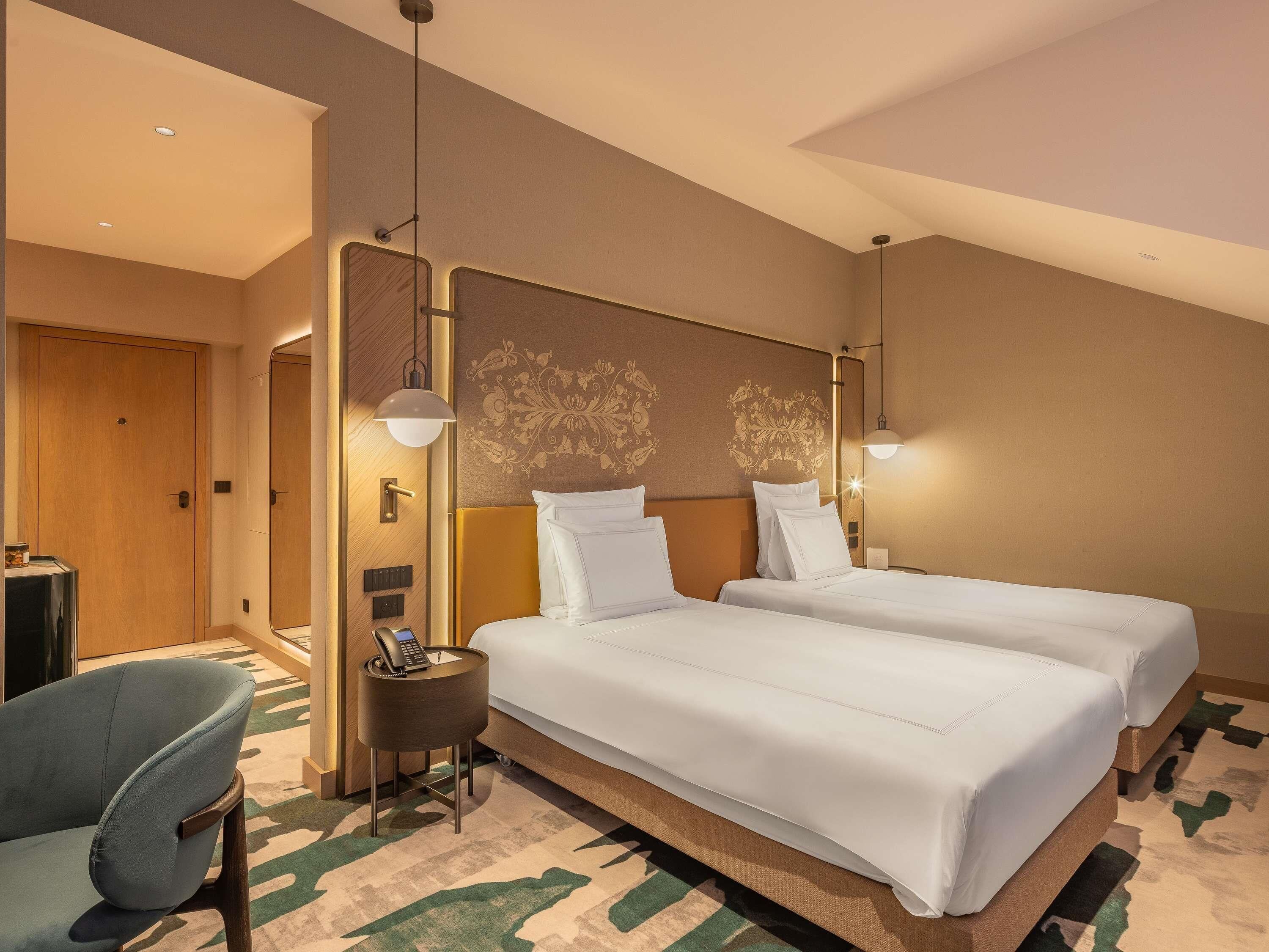 A hotel room with two beds, a desk with a phone, a chair, and a patterned carpet.