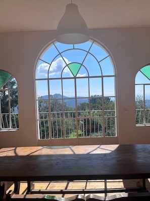 A room with a large arched window, a wooden table, and a view of a mountainous landscape.