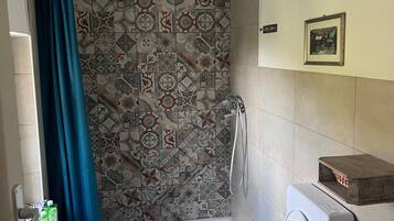 Une salle de bain avec des carreaux décorés, une douche, deux toilettes, un lavabo et une petite étagère.