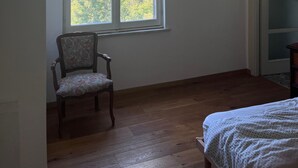 Een kamer met een groot raam, een stoel, een bed en een hanglamp.